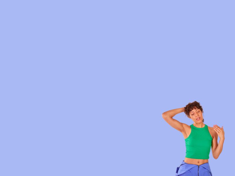 A woman wearing a green tank top and blue pants is holding her hair up and fanning her face