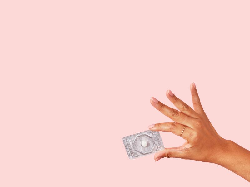 a woman's hand holding emergency contraception on a pink background