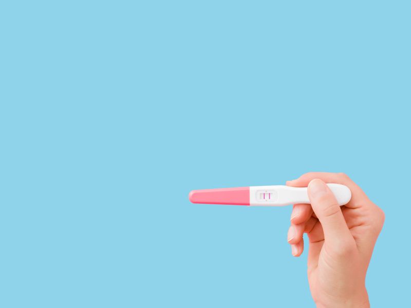 A woman's hand holding a pregnancy test in front of a light blue background