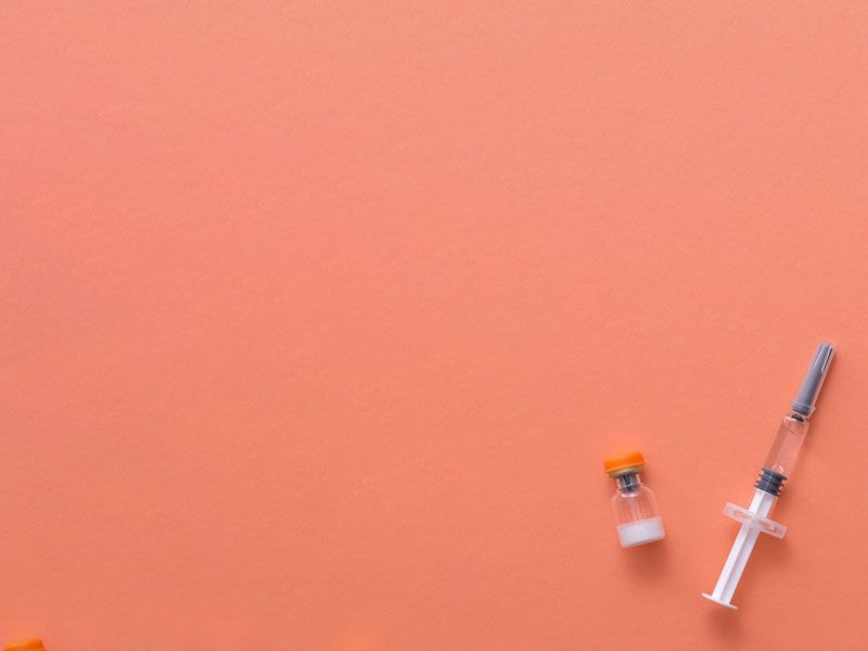 A syringe and vial of liquid on an orange surface