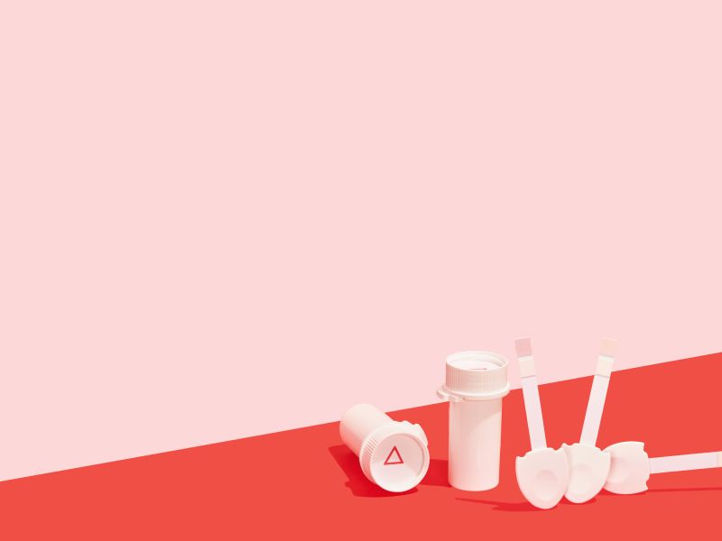 Two Wisp pill vials and 3 urine testing strips on a red surface with a pink background