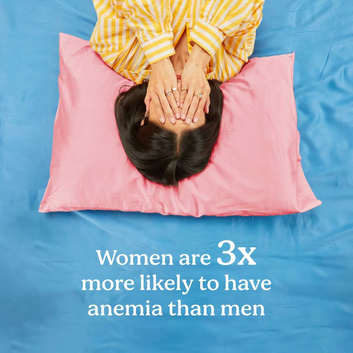 A woman wearing yellow striped pajamas laying down with her hands over her face on a pink pillow with blue bedding