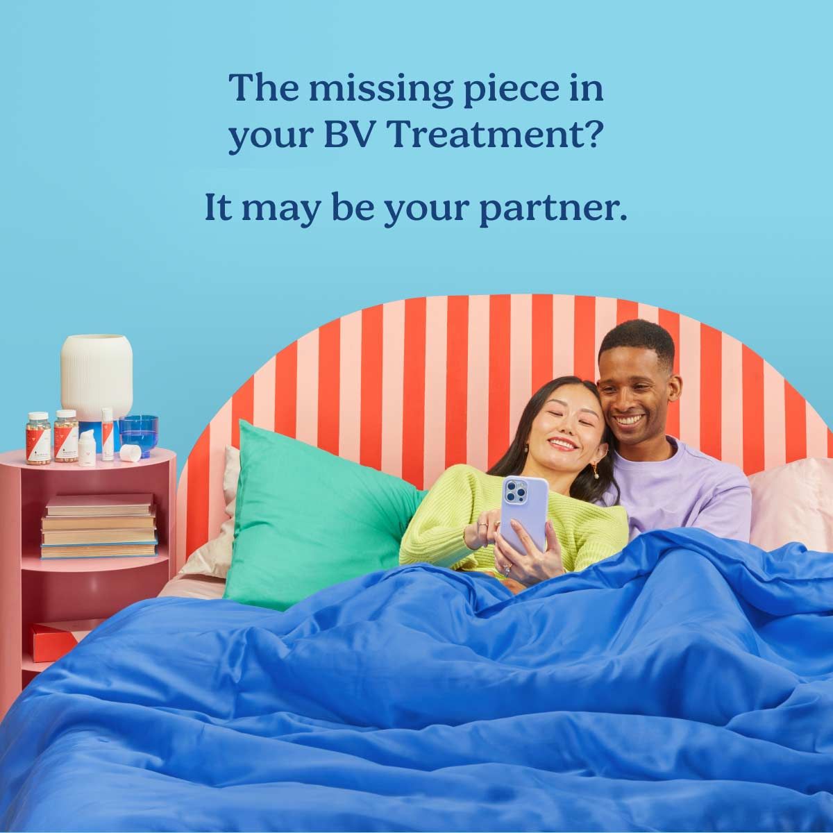 A couple laying in a colorful bed together smiling and looking at a mobile phone