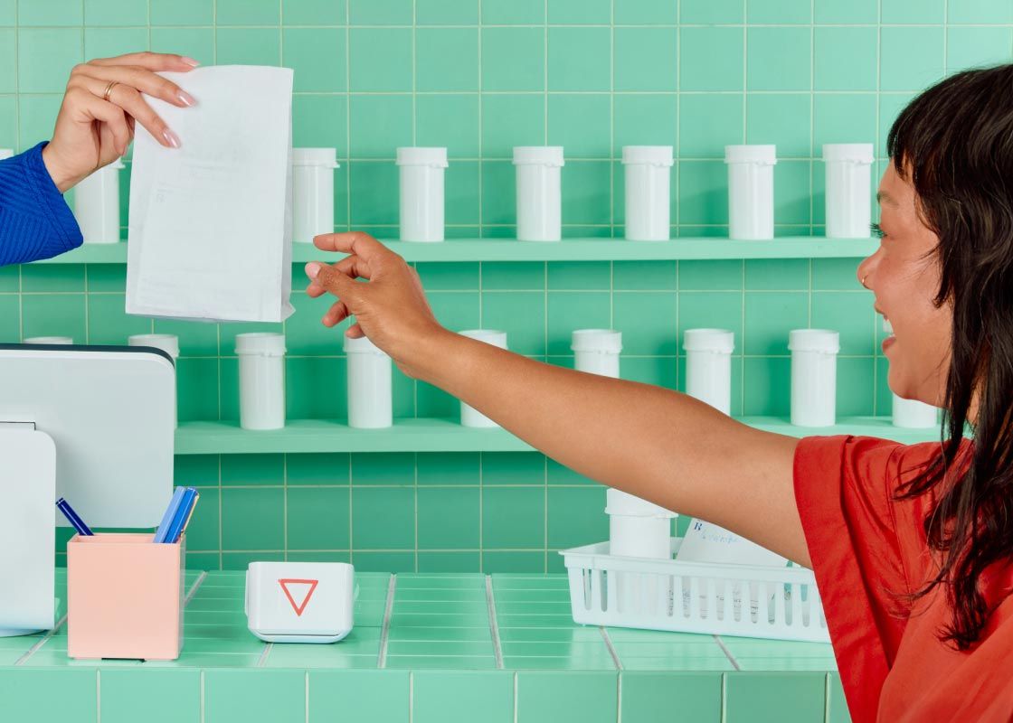 A woman wearing a red blouse is picking up meds at a pharmacy