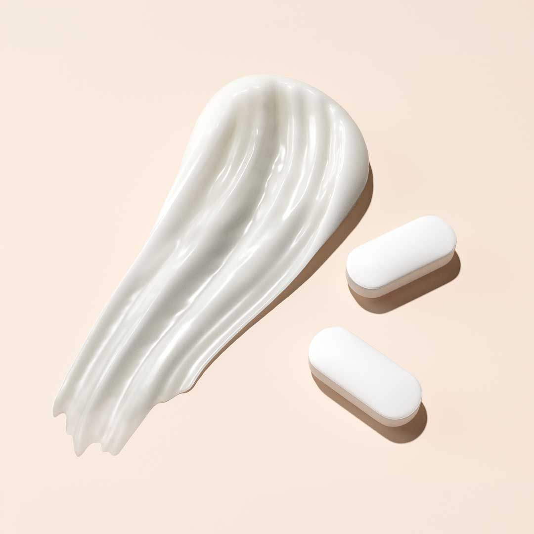 A cream swatch and two pills on a cream surface