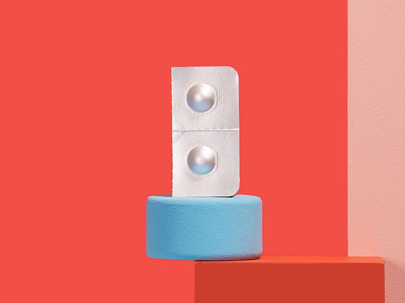 A pill packet of Zofran balanced on colorful abstract shapes in front of a red background