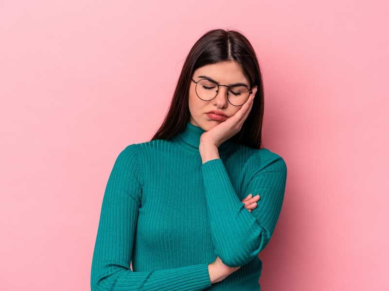 A woman wearing a green sweater and looking tired in front of a pink background