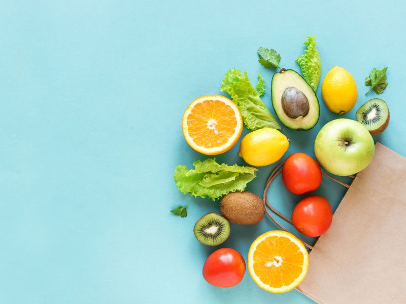 A grocery bag with healthy vegetables and fruits laid out on a light blue surface