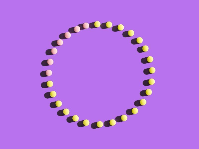 Pink and yellow birth control pills making a circle on a purple surface