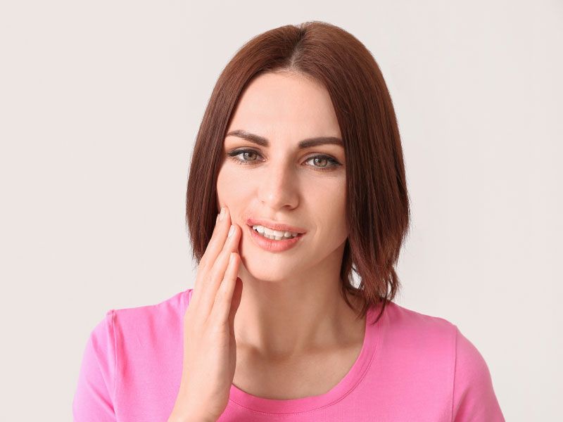 A woman wearing a pink shirt is touching her face with a pained expression