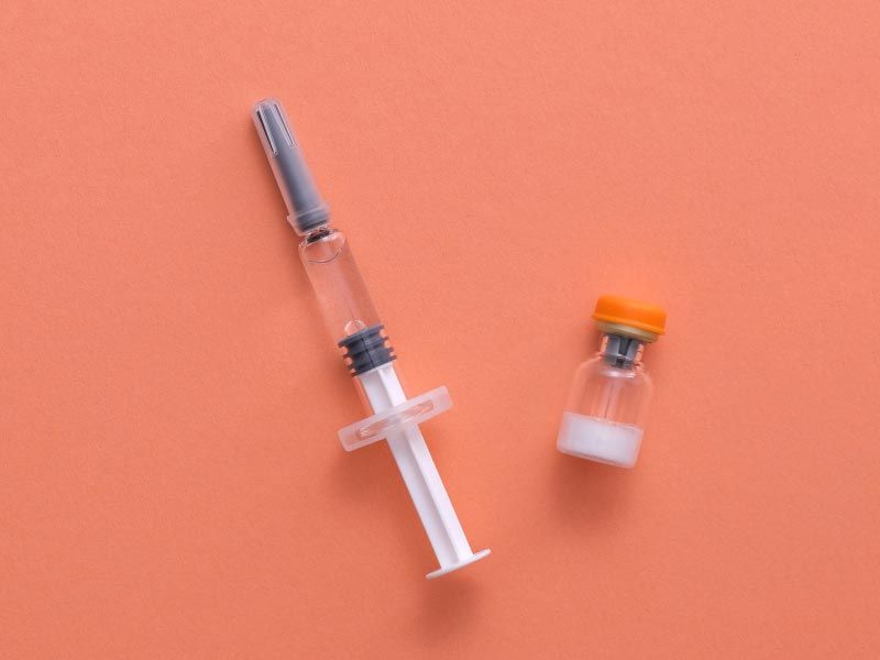 A syringe and vial of liquid on an orange surface