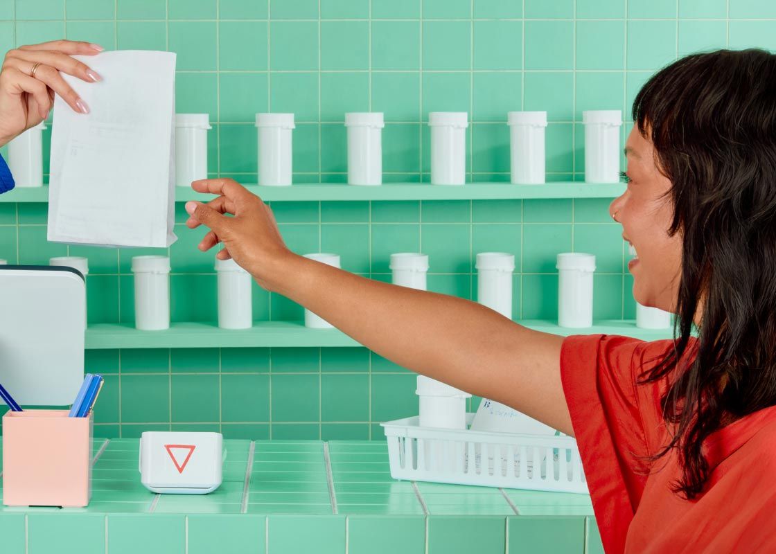 A happy woman wearing a red shirt is picking up Wisp medication at a pharmacy