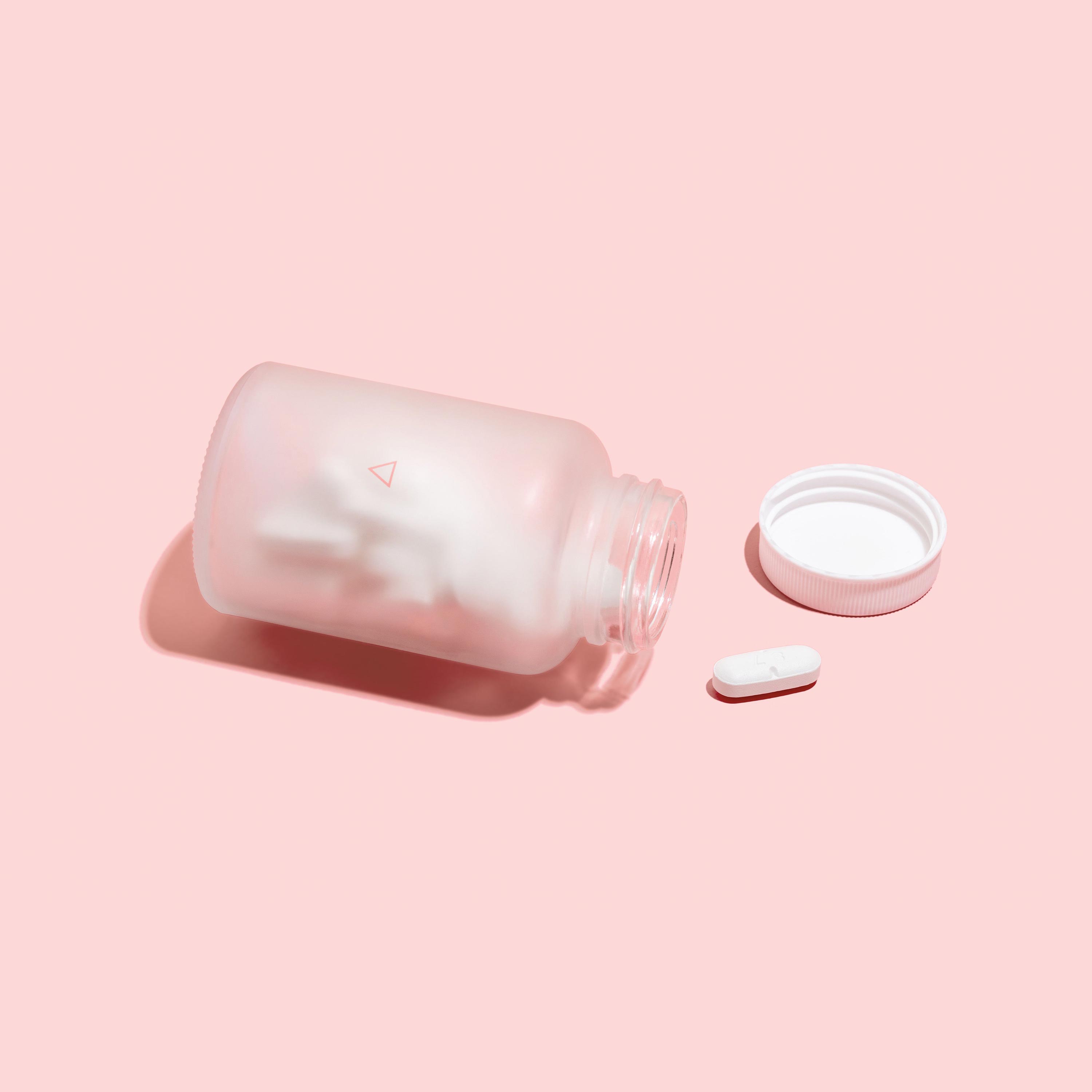 Bottle of Valacyclovir open on its side, on a pink background