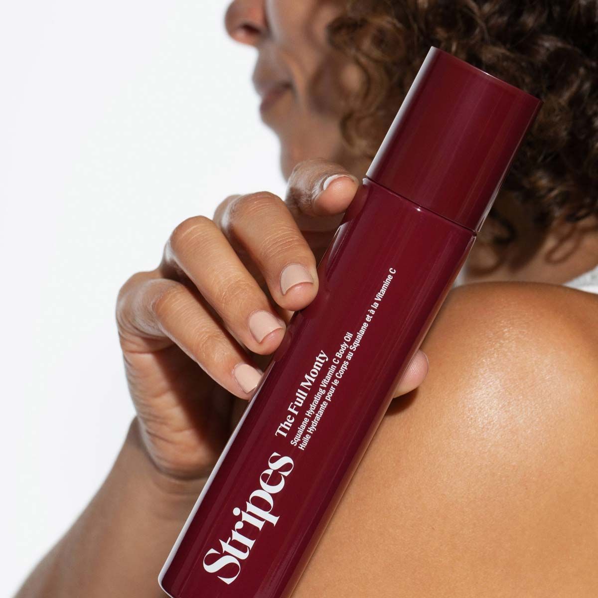 A woman holding a bottle of The Full Monty by Stripes Beauty